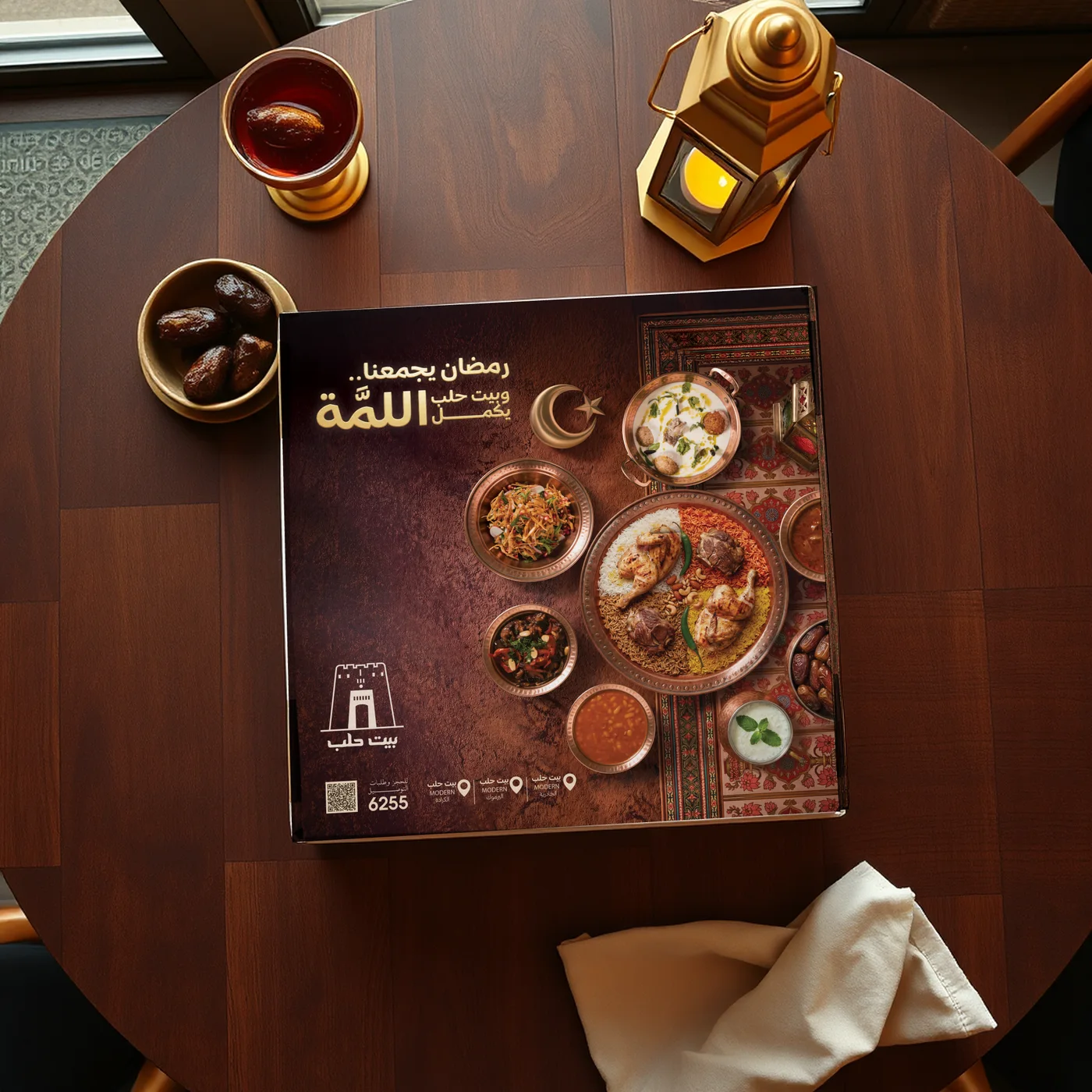 Square Ramadan box with the full key visual on its lid, on a restaurant table beside dates, tea and a lantern